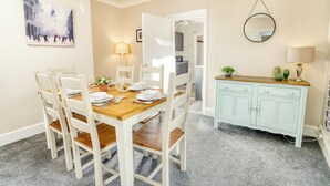 A dining area with a wooden table and white chairs, a light blue cabinet, and a painting on the wall. - Corner House, close to Lincoln City Centre (Lincoln)