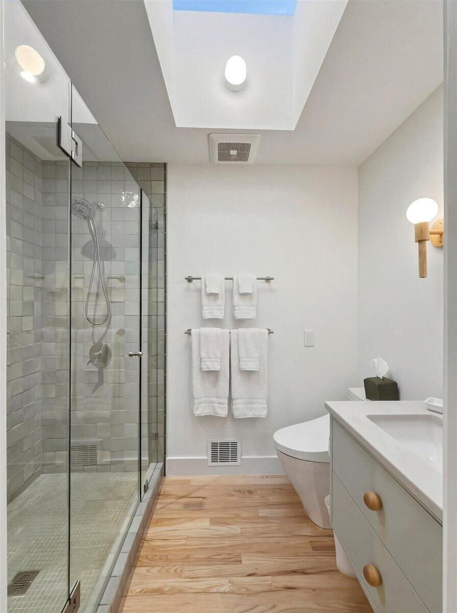 A bright, modern bathroom with a walk-in tiled shower, skylight, and Toto bidet for added comfort.