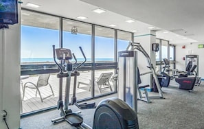 Ein Fitnessstudio mit Cardiogeräten, Krafttrainingsmaschinen und Meerblick durch große Fenster.
