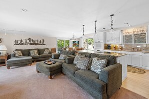 Ein Wohnzimmer mit Ecksofa, Hocker und einem Essbereich mit Stühlen.