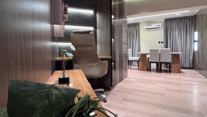 Un espacio de oficina moderno con un escritorio de madera, una silla cómoda, una planta verde grande y una zona de comedor con una mesa y sillas.