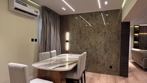 Un área de comedor moderna con una mesa de mármol, sillas tapizadas, iluminación empotrada y un aire acondicionado de pared.