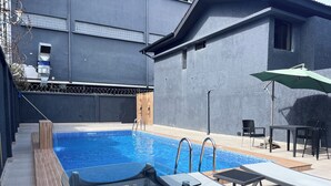 Una piscina con cubierta de madera, sillas de descanso y una mesa.