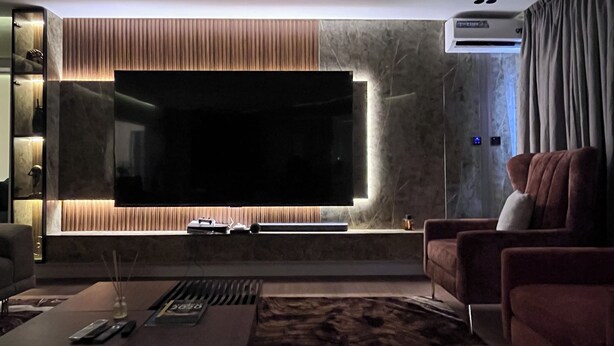 Una sala moderna con un televisor de pantalla plana grande, un sofá, una mesa de centro con mandos a distancia y un aire acondicionado.
