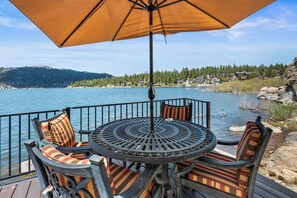 A deck with a table and chairs, overlooking a lake with houses in the background.