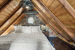 A bedroom with a stone wall, wooden beams, a bed, and a hanging light fixture.