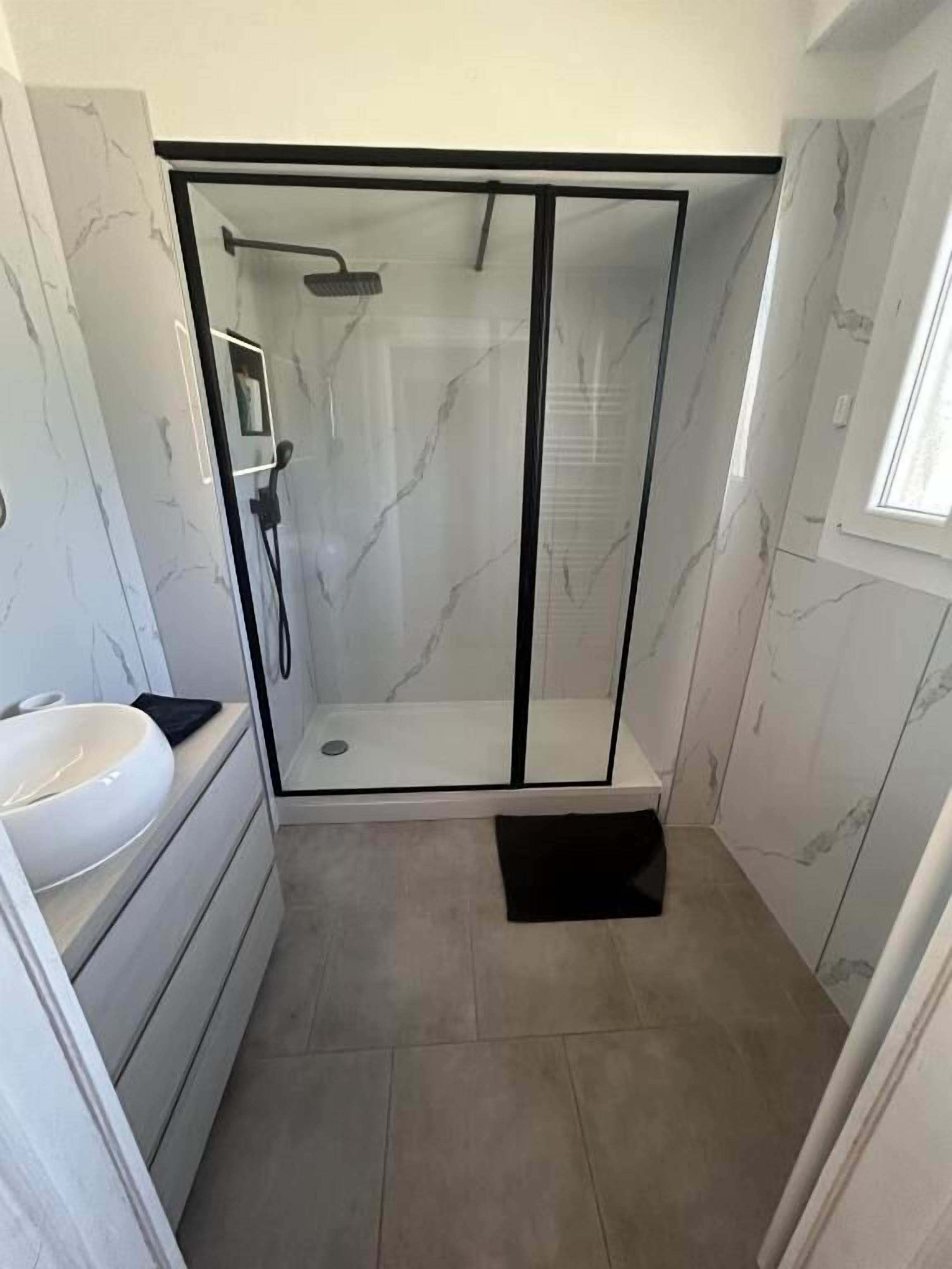 A bathroom with a glass-enclosed shower, a white sink, and marble walls.