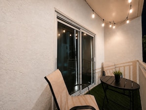 A patio with a sliding glass door, a round table with a potted plant, and string lights.