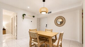 Een eetruimte met een houten tafel en stoelen, een hanglamp en een spiegel aan de muur.