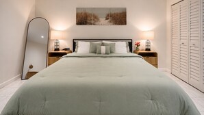 Een slaapkamer met een bed, twee nachtkastjes met lampen, een grote spiegel, een wanddecoratie en een kledingkast.