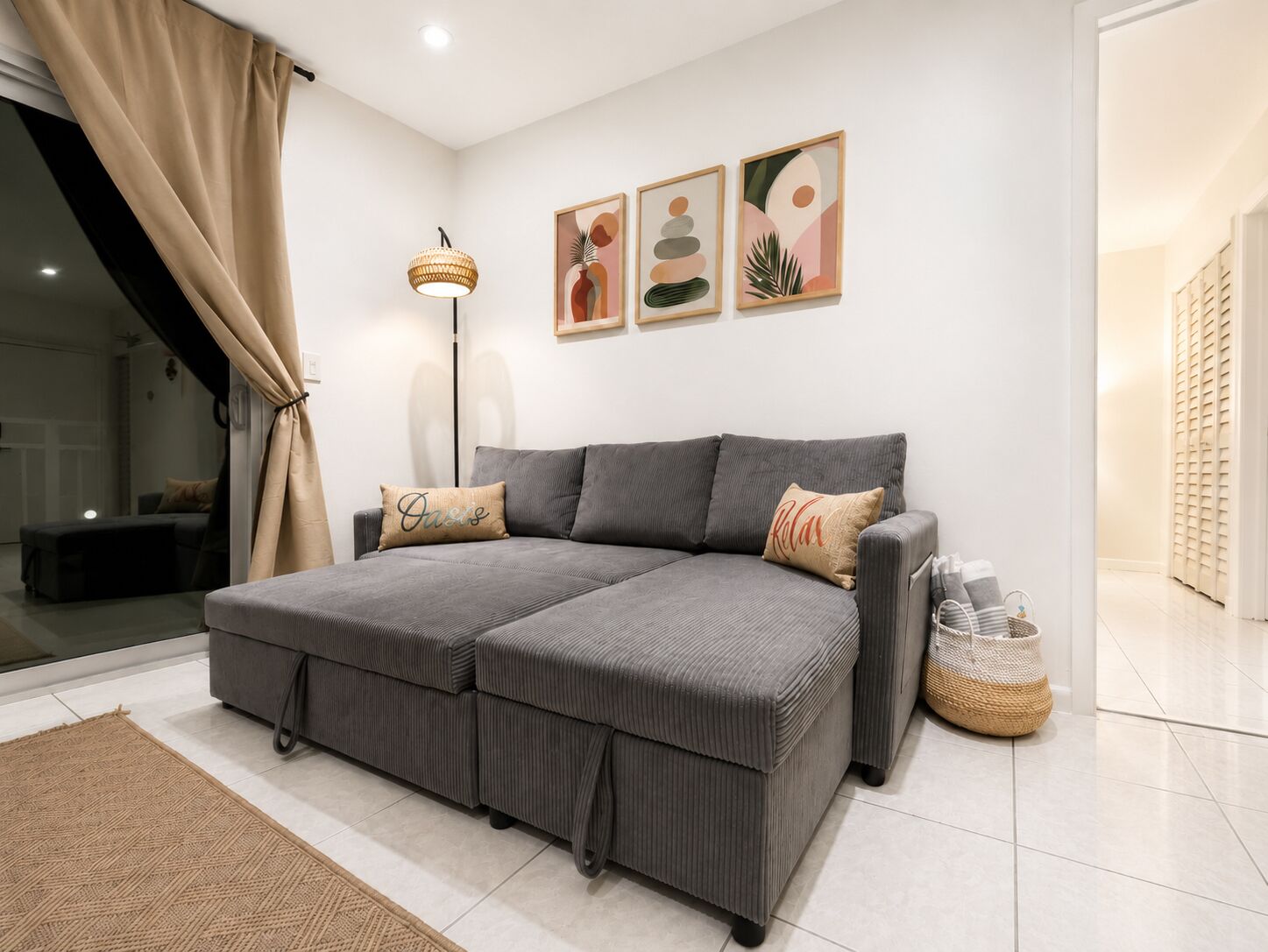 A modern bedroom with a grey sofa bed, a floor lamp, and abstract wall art.