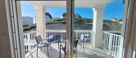 A balcony with a view of a beach and houses, featuring a table and chairs.