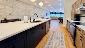 Una cocina moderna con pared de ladrillo blanco, armarios negros, una isla grande e iluminación colgante.