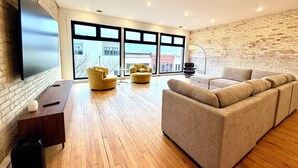 Un salón moderno con una televisión grande, dos sillones amarillos, un sofá beige y una pared de ladrillo.