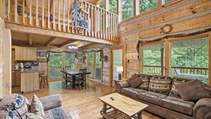 Une cabine spacieuse avec un intérieur en bois, un balcon, un coin repas et une grande fenêtre donnant sur la forêt.