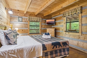A wooden cabin room with a bed, a television, and windows with curtains. - Black Bear Hideaway 2 Bedroom Home (Sevierville)