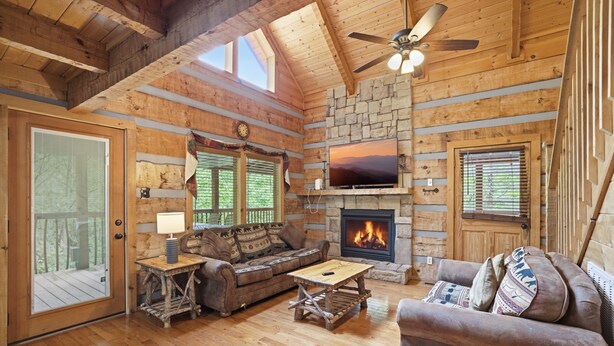 L’intérieur d’une cabane en rondins, avec une cheminée, des meubles en bois et un ventilateur de plafond.