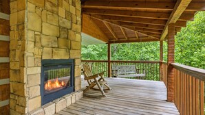 Une terrasse couverte avec une cheminée en pierre, des fauteuils à bascule en bois et une vue sur une forêt.