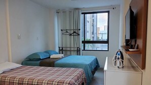 Habitación de hotel con dos camas, televisión, escritorio con ordenador y ventana con vista a la ciudad.