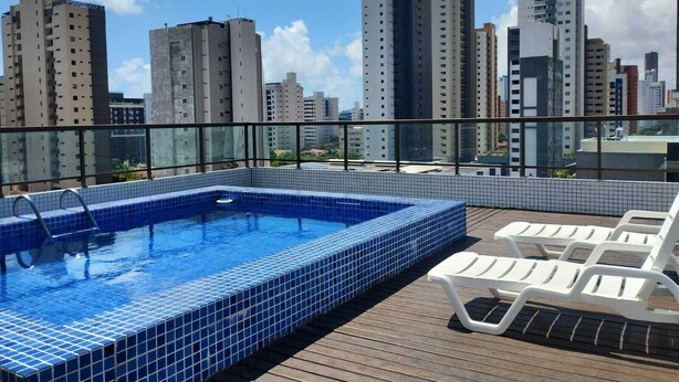 Una piscina en la azotea con azulejos azules, sillones blancos para tomar el sol y vistas panorámicas de la ciudad.