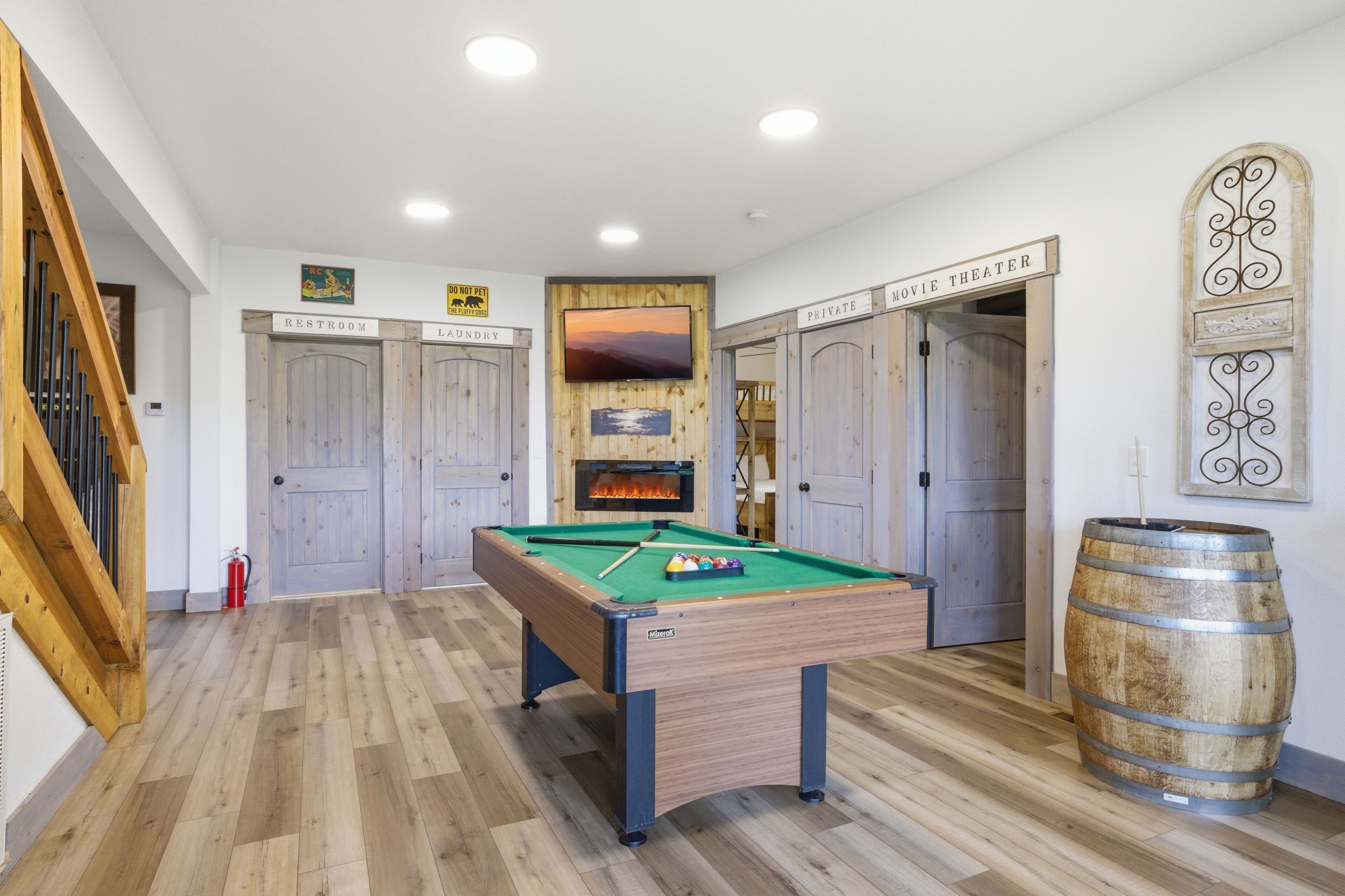 A pool table in a room with wooden flooring, a fireplace, and doors labeled 'Restroom' and 'Private Movie Theater.'