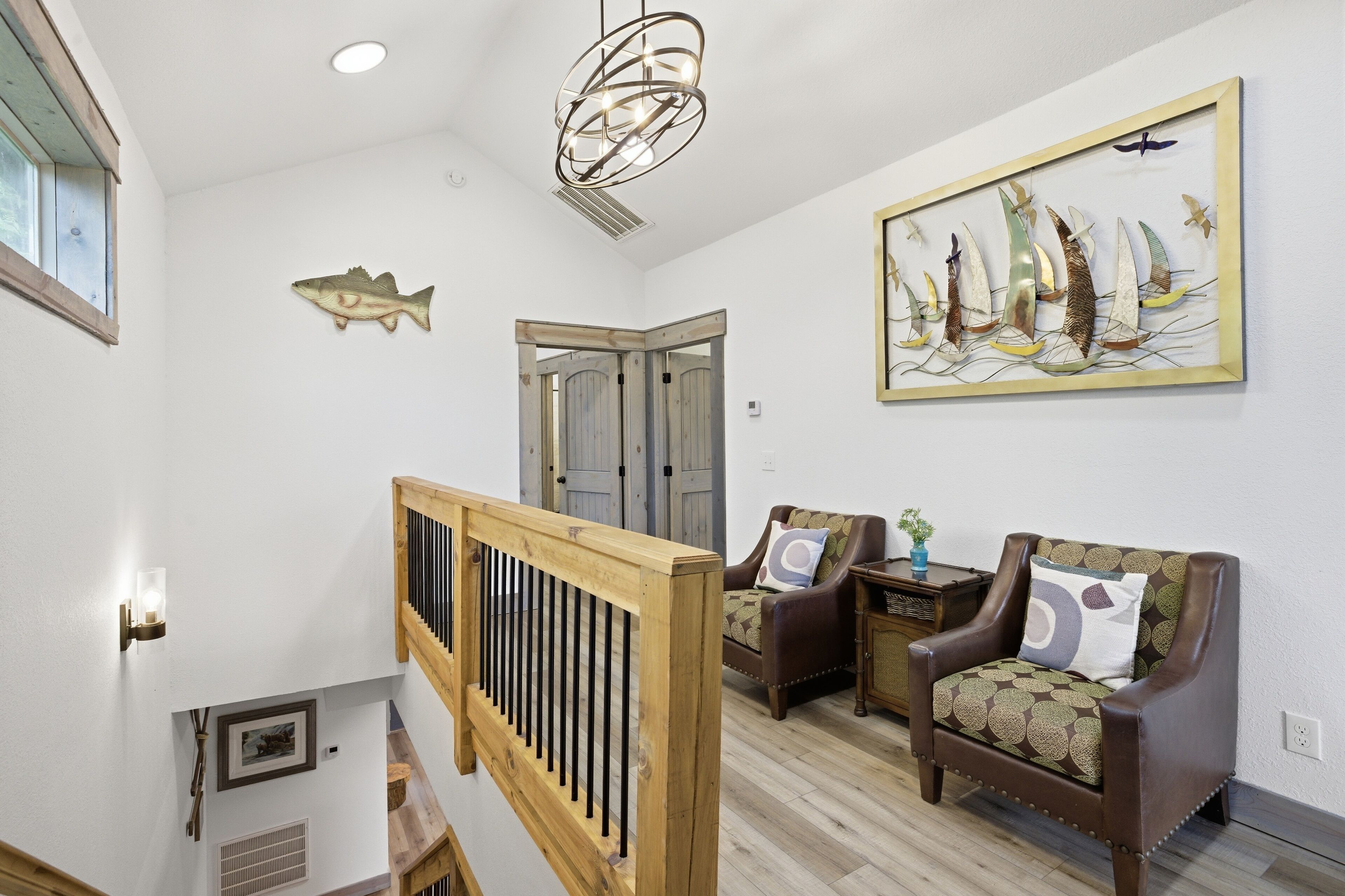Une pièce avec un escalier en bois, un canapé en cuir marron, une décoration murale représentant des poissons et un tableau représentant un voilier.