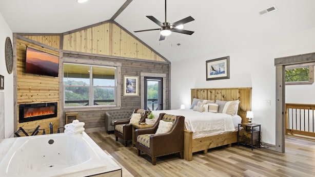 Un dormitorio con una cama grande, ventilador de techo, chimenea y vistas al exterior.