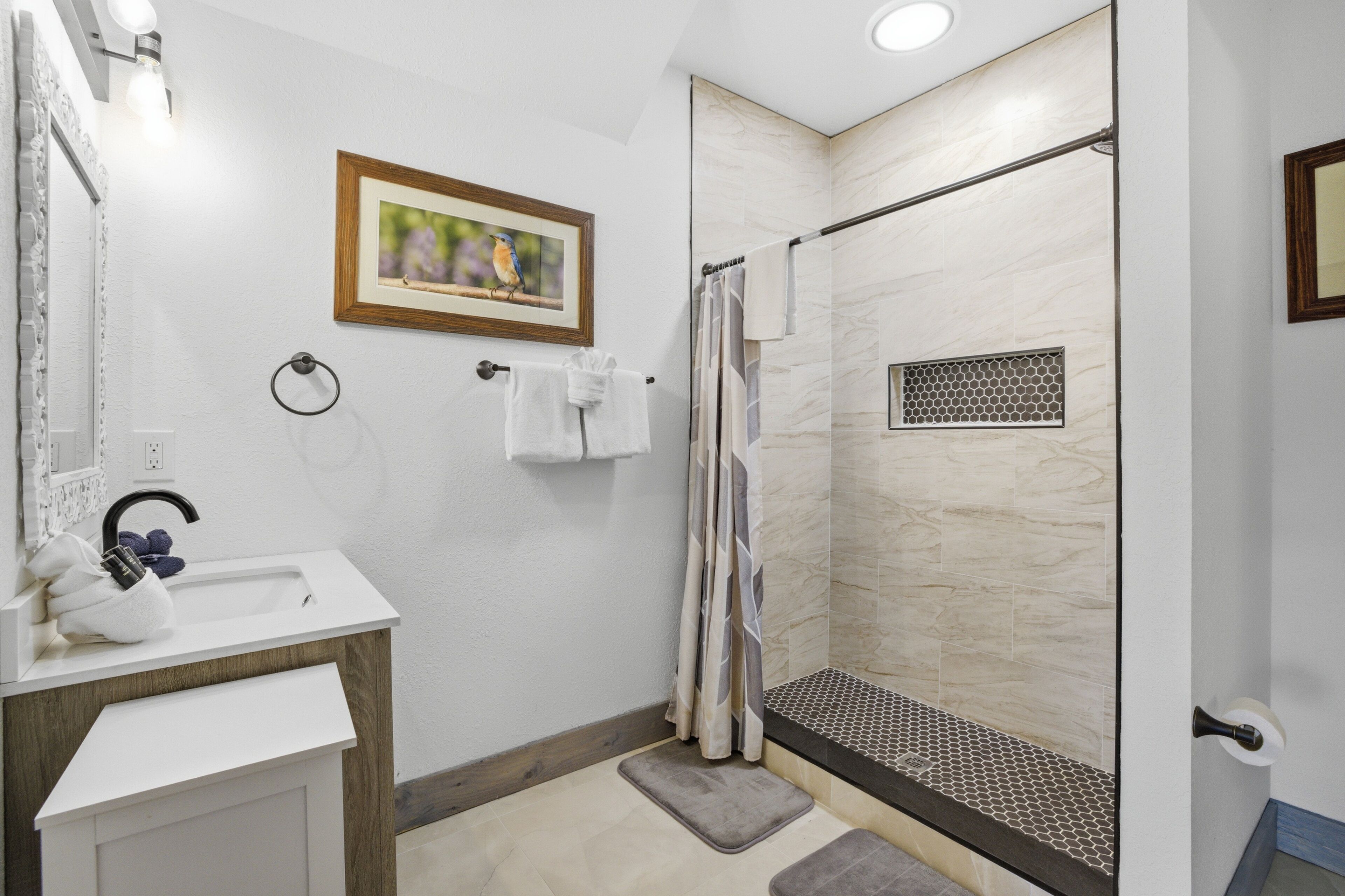 A bathroom with a sink, mirror, towel rack, shower with a glass door, and a framed picture on the wall.