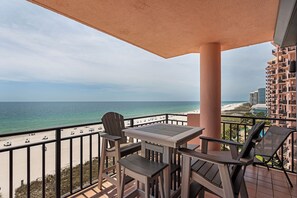 Ein Balkon mit Blick auf Strand und Meer, Holzmöbel und ein Hochhaus im Hintergrund.