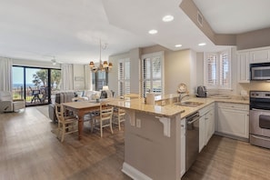A modern kitchen with a central island, white cabinetry, and a dining area with a table and chairs. - 0105W-3 bedroom unit located on the 1st floor (Orange Beach)