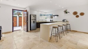 A modern kitchen with a central island, bar stools, a refrigerator, and a microwave. - Tulum Paradise | 4BR Home with Private Pool (Tulum)