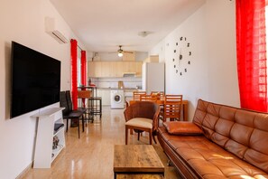 Uma sala de estar moderna com uma TV de tela plana, um sofá de couro marrom, uma mesa de centro de madeira e um espaço de jantar com uma cortina vermelha.