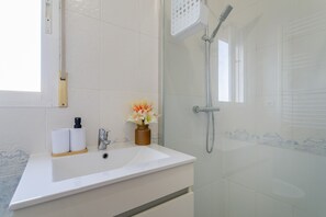 Casa de banho com lavatório branco, chuveiro e janela.