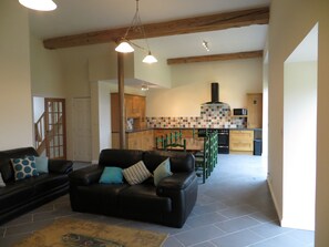 Ein Wohnzimmer mit einer schwarzen Ledersofa, einem Holzespeisetisch und einer Küche mit Holzschränken und einer gefliesten Spritzschutzwand.