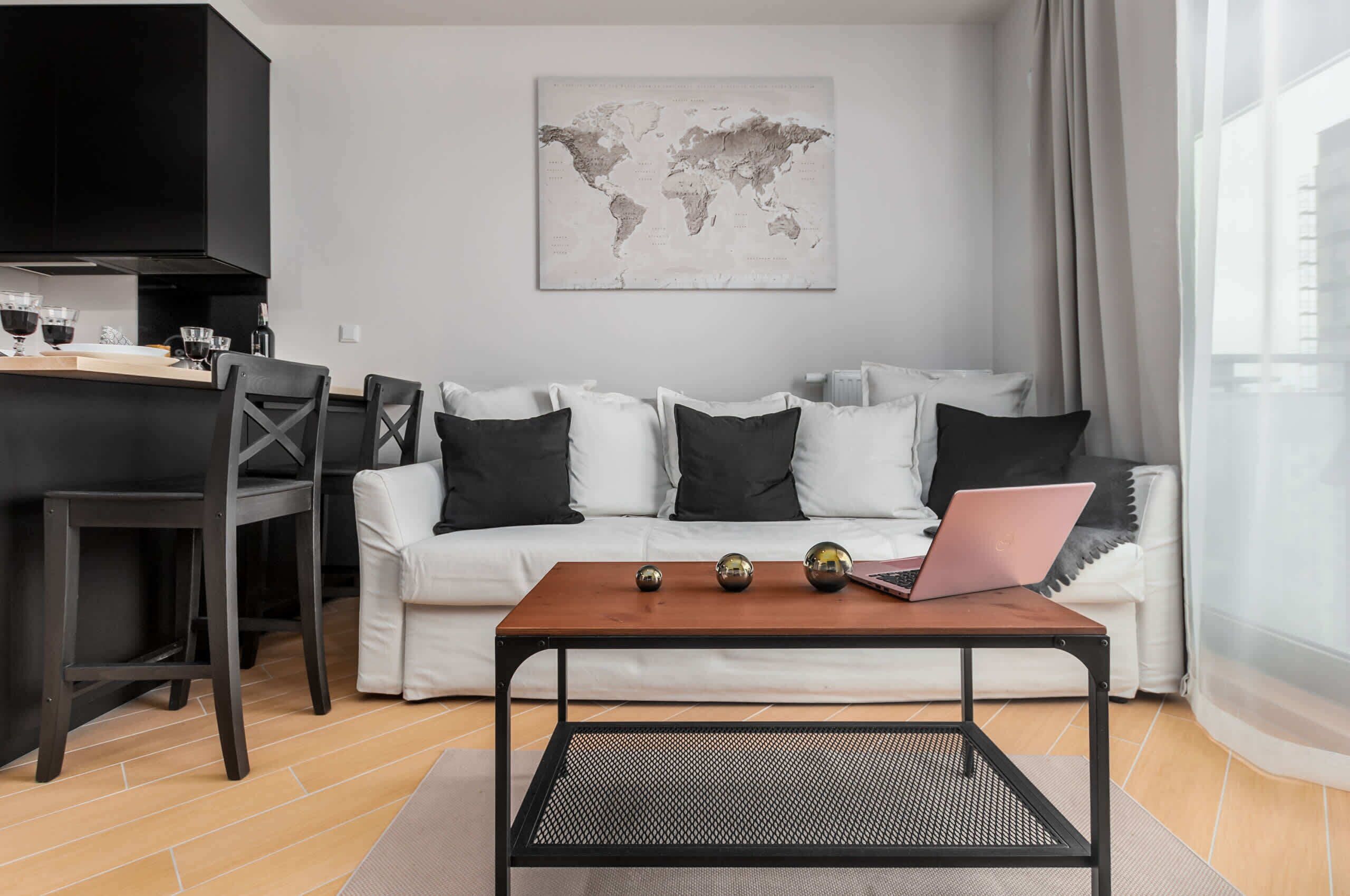 Ein modernes Wohnzimmer mit einem weißen Sofa, schwarz-weißen Kissen, einem Holztisch und einem Laptop.