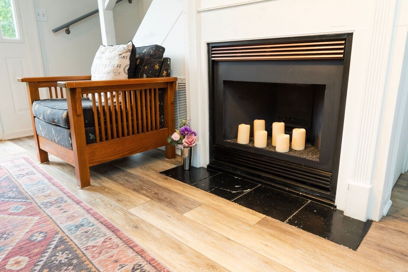 A living room with a wooden bench, a fireplace with candles, and a patterned rug.