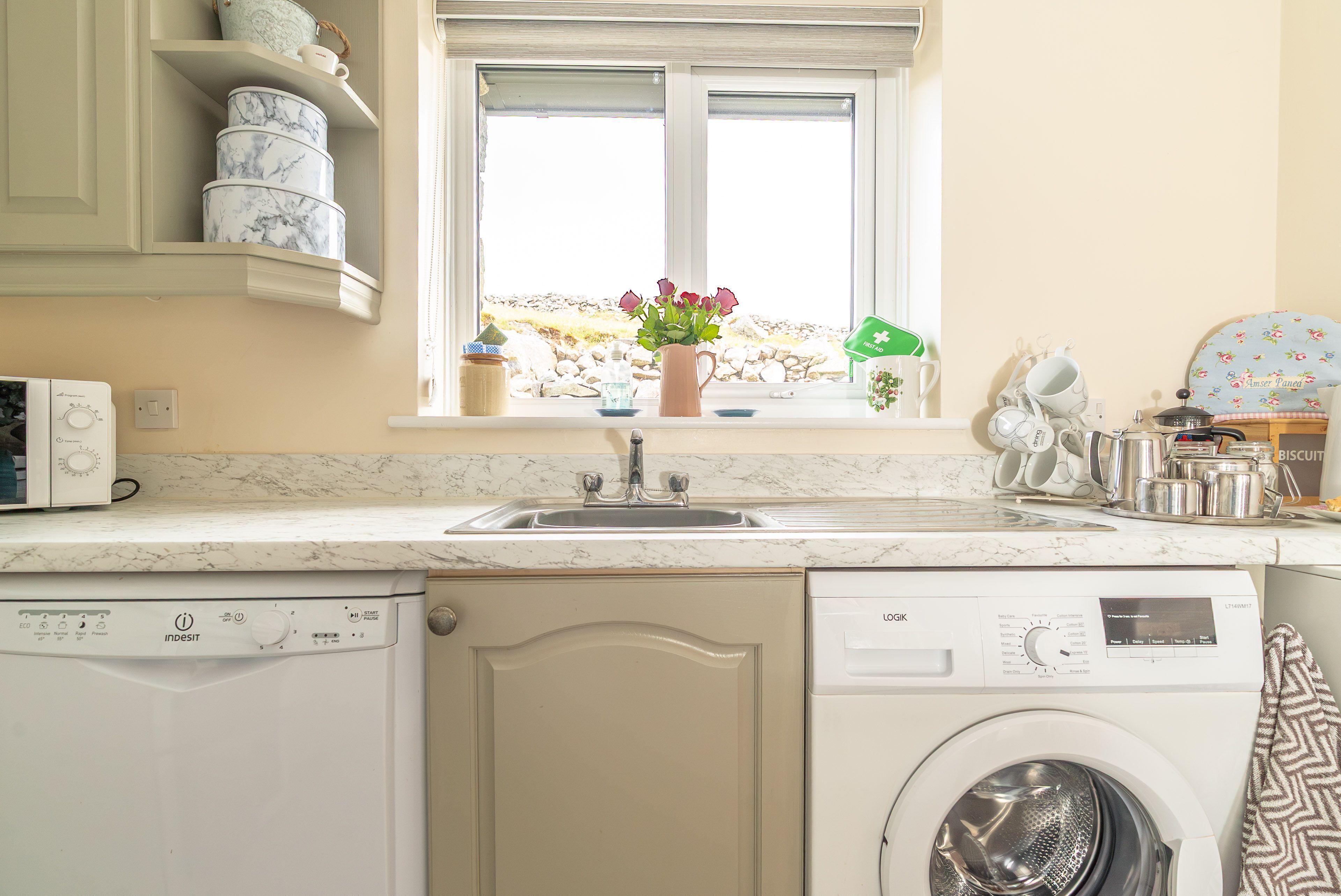A kitchen with a sink, a washing machine, a microwave, and a window with a view of rocks.