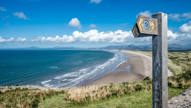 Un paisaje costero con un letrero de madera, una playa y un cielo azul despejado.