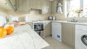Una cocina con encimera de mármol, microondas, horno, lavavajillas y ventana con flores.