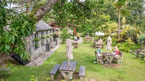 Ein Garten mit Steinmauern, hölzernen Bänken und Tischen unter Bäumen.