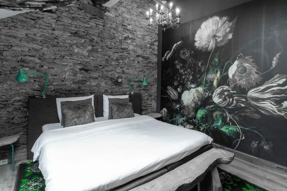 Un dormitorio con pared de piedra, cama con ropa blanca, candelabro y un mural floral.