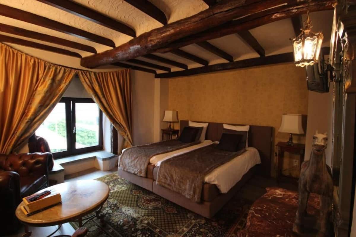 Un dormitorio con una cama grande, dos mesitas de noche con lámparas, una ventana con cortinas y techo de madera.
