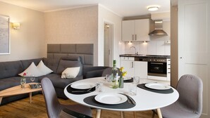 Un salon moderne avec un canapé, une table à manger dressée pour deux personnes et une cuisine en arrière-plan.