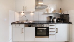 Une cuisine moderne avec des meubles blancs, un plan de travail noir, un four encastré et une machine à café.