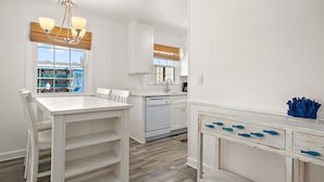 A kitchen with white cabinetry, a white dining table, and a white countertop with blue fish-shaped handles. - Great Location for Family fun at Jolly Roger and Boardwalk! (Ocean City)