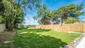 A backyard with a wooden fence, a lawn, and trees. - Lovingly renovated barn near the Lon Goed | Llwyn-Y-Forwyn (Chwilog)