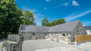 A stone building with a gravel driveway and a wooden fence. - Lovingly renovated barn near the Lon Goed | Llwyn-Y-Forwyn (Chwilog)