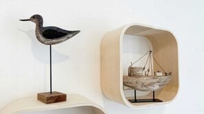 Une sculpture d’oiseau sur un socle en bois, une chaise en osier et une balance fixée au mur.