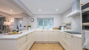 A modern kitchen with white cabinetry, a herringbone wood floor, a window with vertical blinds, and a built-in oven. - Beautifully Converted Workshop Close to the Beach | Gweithdy-Bronafon (Borth y Gest)