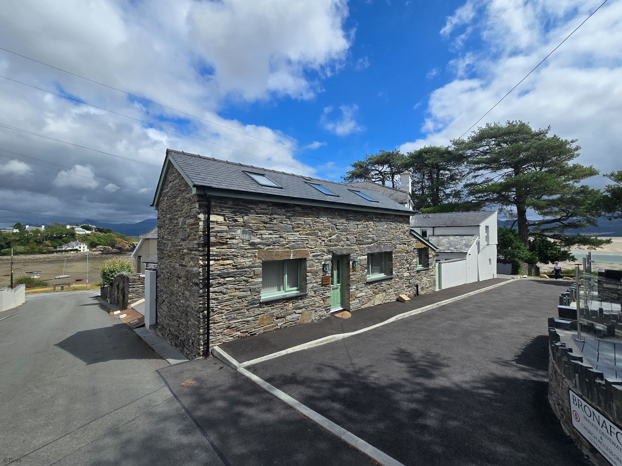 A stone building with a sloped roof, a driveway, and a parking area.